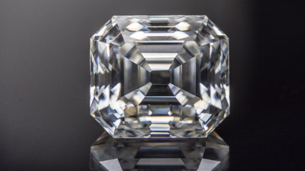 An Asscher-cut diamond, showcasing its unique stepped facets and brilliant sparkle, resting on a dark, reflective surface.