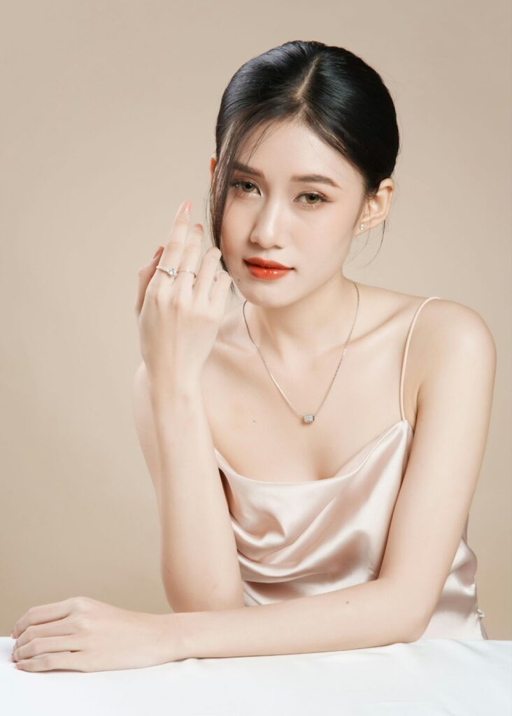 Elegant woman wearing a satin dress, showcasing a delicate necklace and stylish rings, radiating sophistication and timeless beauty