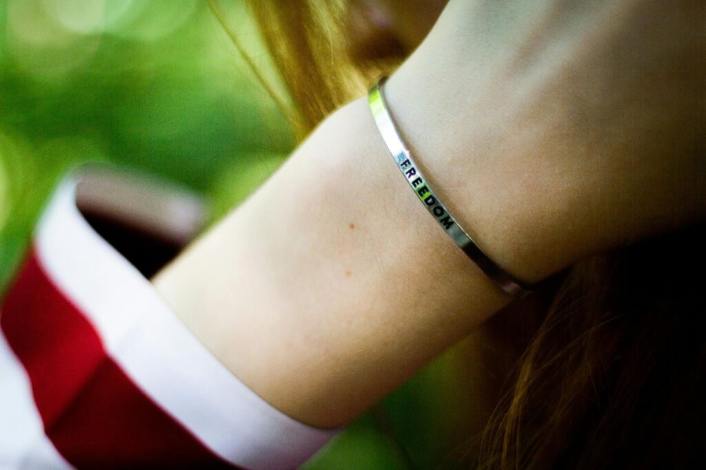 A close-up of a wrist wearing a silver bracelet engraved with the word "Freedom".