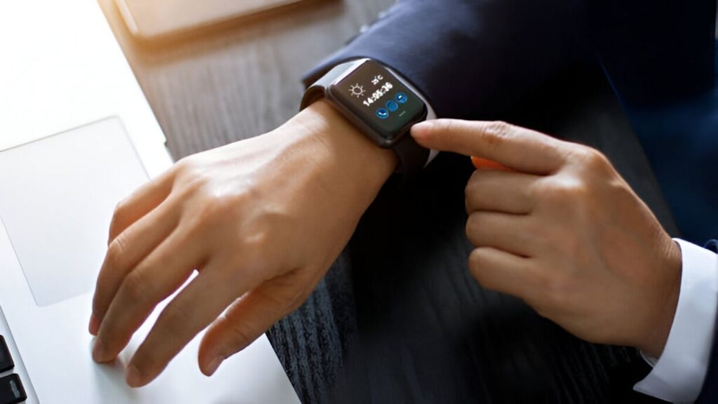 A businessman interacts with his smartwatch while working on a laptop.