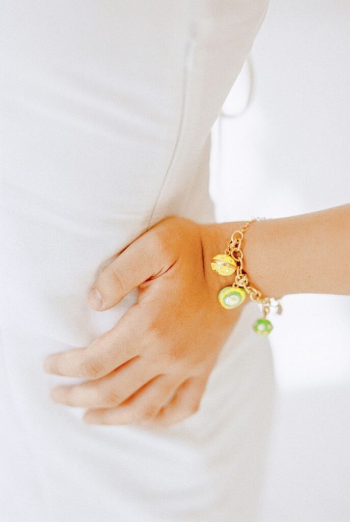 A hand adorned with a colorful charm bracelet, resting against a white background.