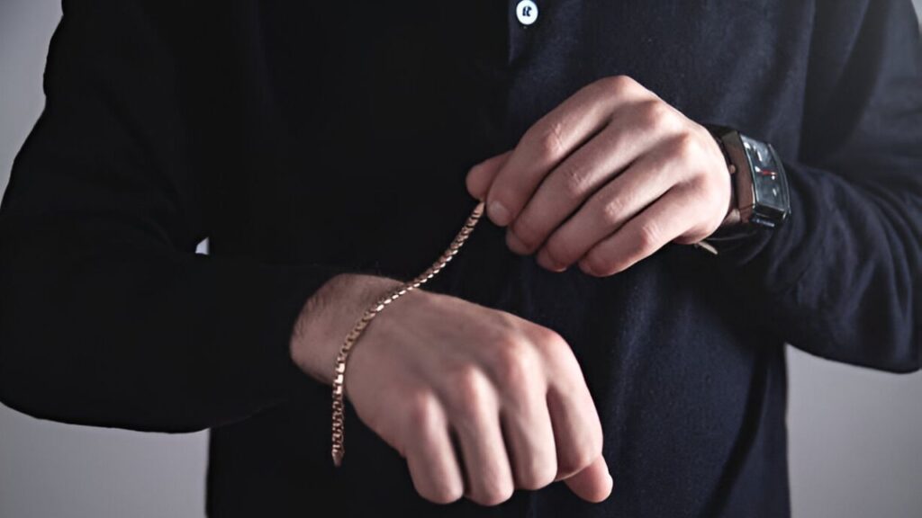 A man adjusting a gold chain bracelet on his wrist.