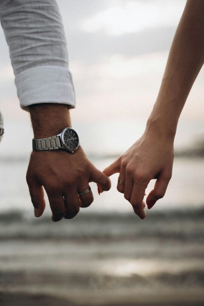 Two hands intertwined, symbolizing love and connection, with a watch on one wrist and a ring on the other.