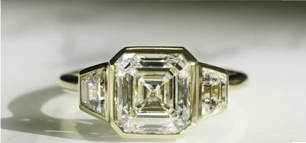 A three-stone ring featuring a large, emerald-cut diamond flanked by two trapezoid-shaped diamonds, set in a gold band.