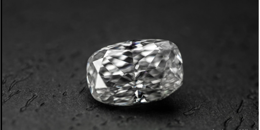 A large, cushion-cut diamond sparkles with intricate facets against a dark, textured background.