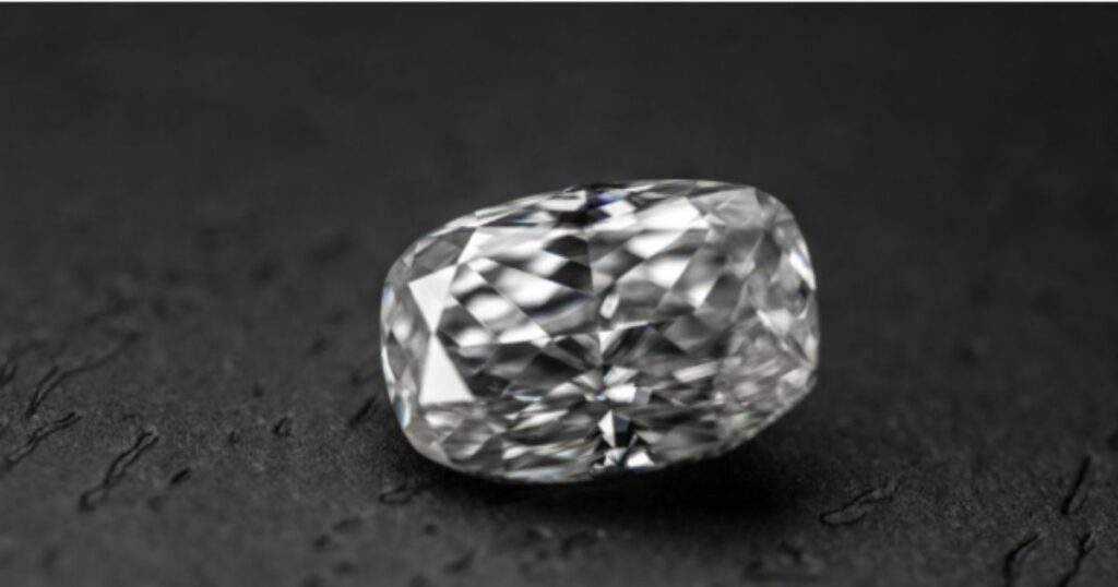 A large, cushion-cut diamond with a unique, slightly irregular shape, sparkling against a dark, textured background.