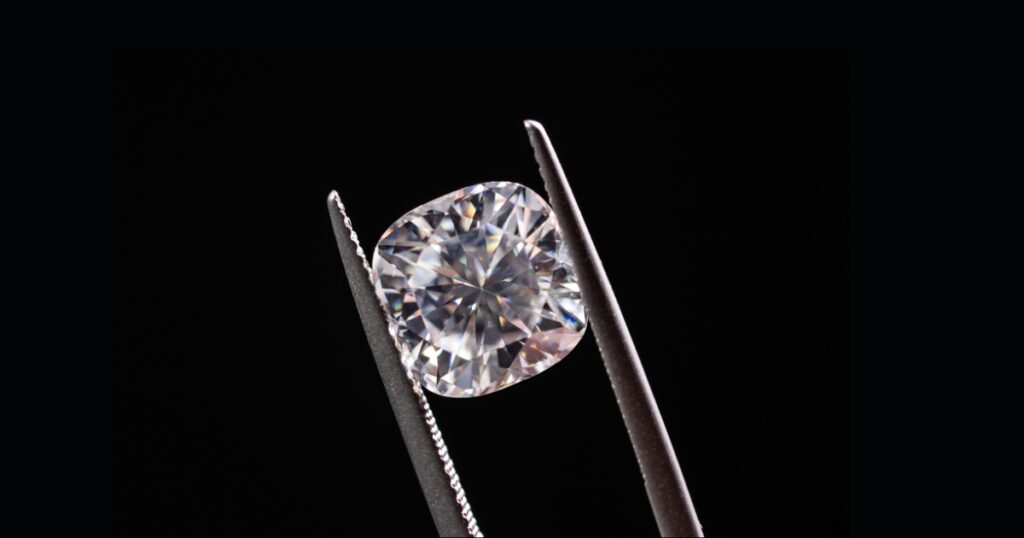 A sparkling, heart-shaped diamond held by metal tweezers against a stark black background.