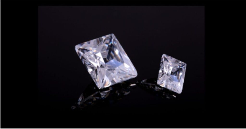 Two rectangular diamonds, one larger, sparkle with reflected light against a dark, glossy background.