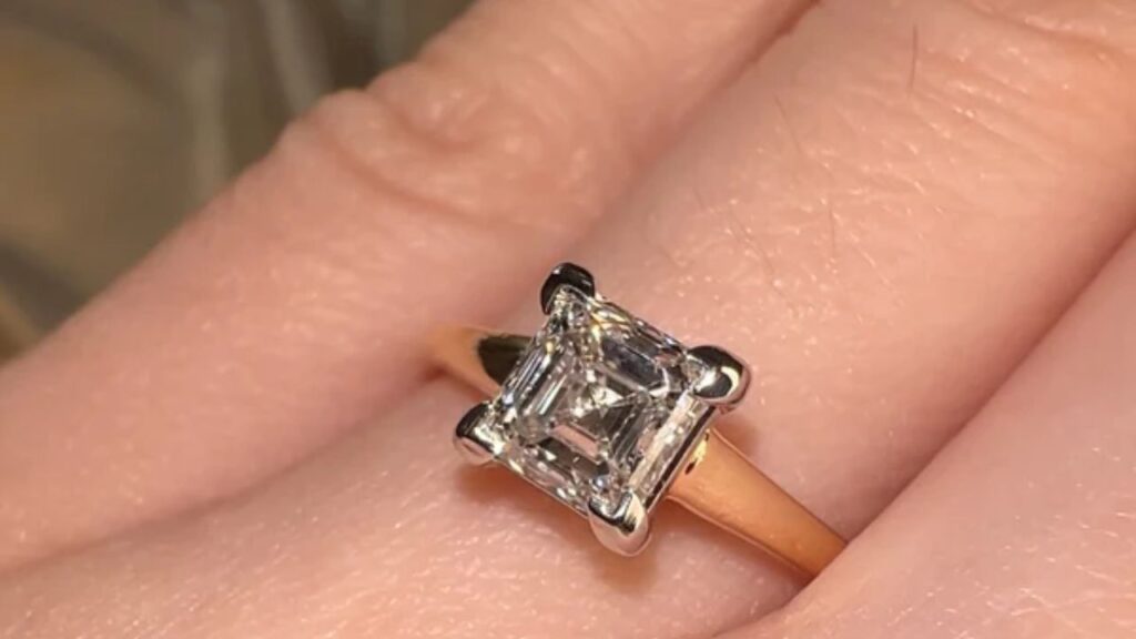 An oval-cut diamond engagement ring with a halo of smaller diamonds and a pave band, displayed against a dark gray background.