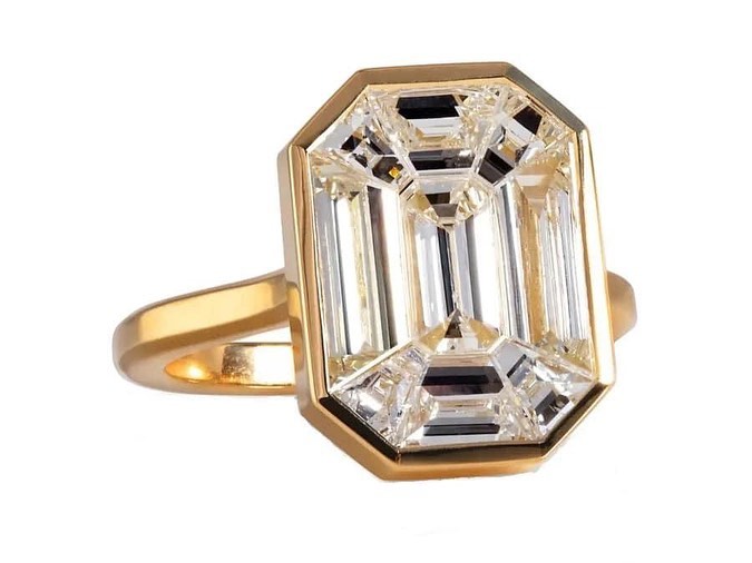 A gold ring showcasing a large, emerald-cut diamond in a bezel setting, displayed on a white background.