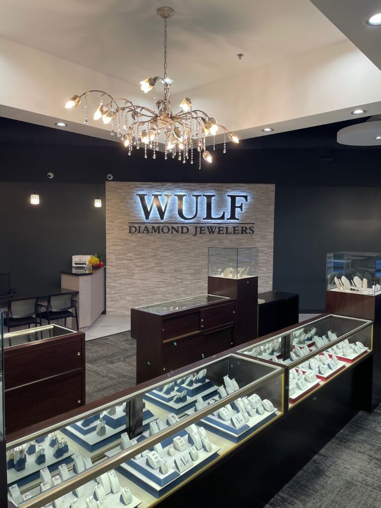 Interior of Wulf Diamond Jewelers with display cases filled with sparkling jewelry under a chandelier and recessed lighting.