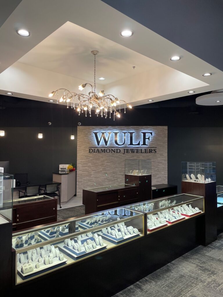 A jewelry store interior with display cases filled with jewelry, a chandelier, and the Wulf Diamond Jewelers sign on the back wall.