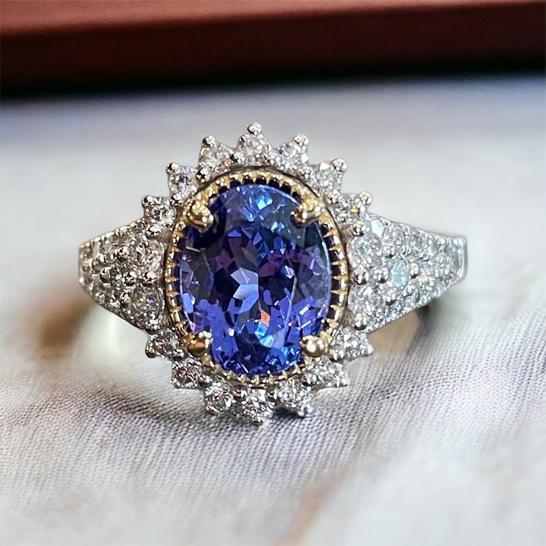 A platinum ring featuring a large, oval-shaped tanzanite gemstone surrounded by a halo of diamonds and smaller diamonds embedded in the band.