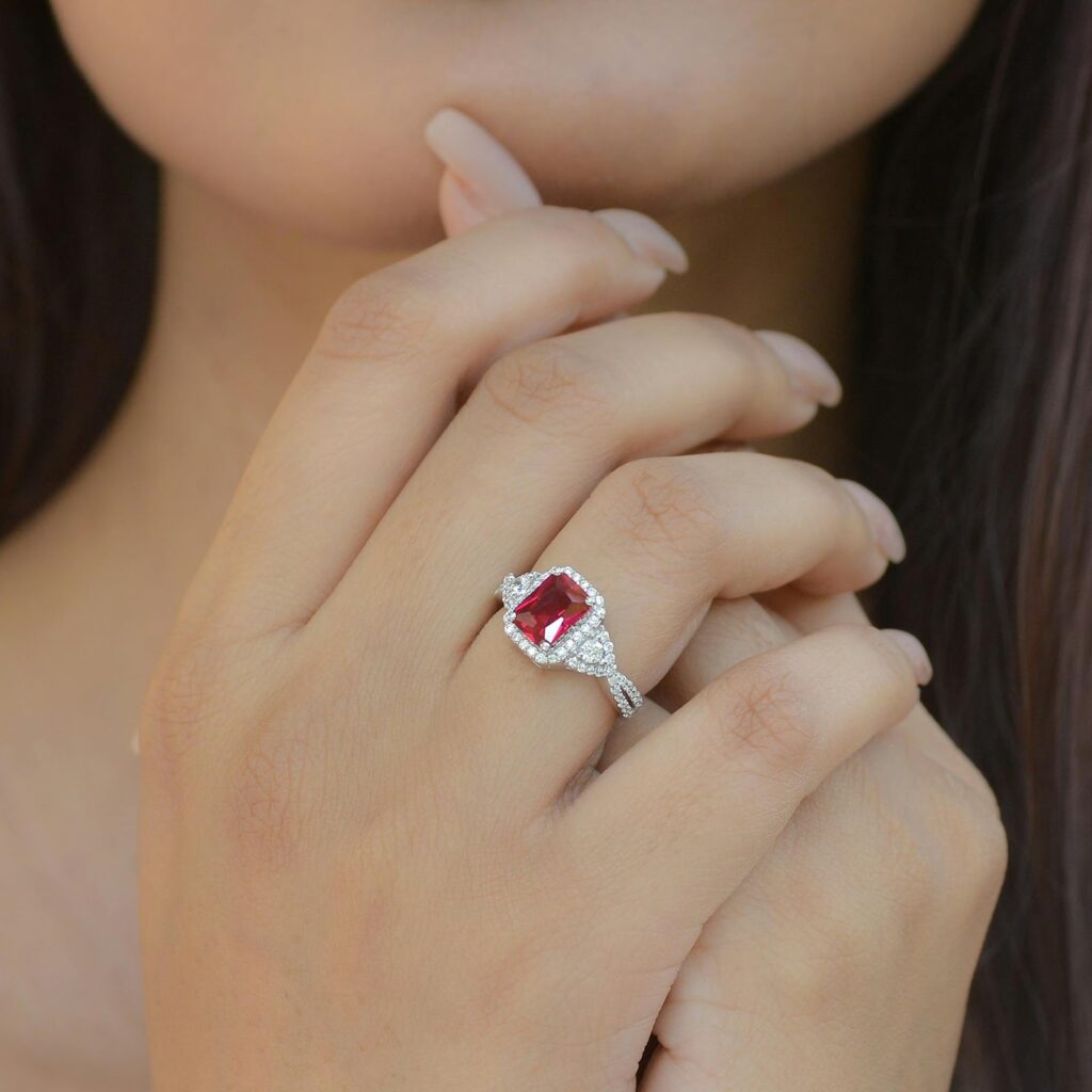 Elegant ruby and diamond halo ring on a woman's hand, featuring a vibrant red gemstone set in a sparkling white gold band.