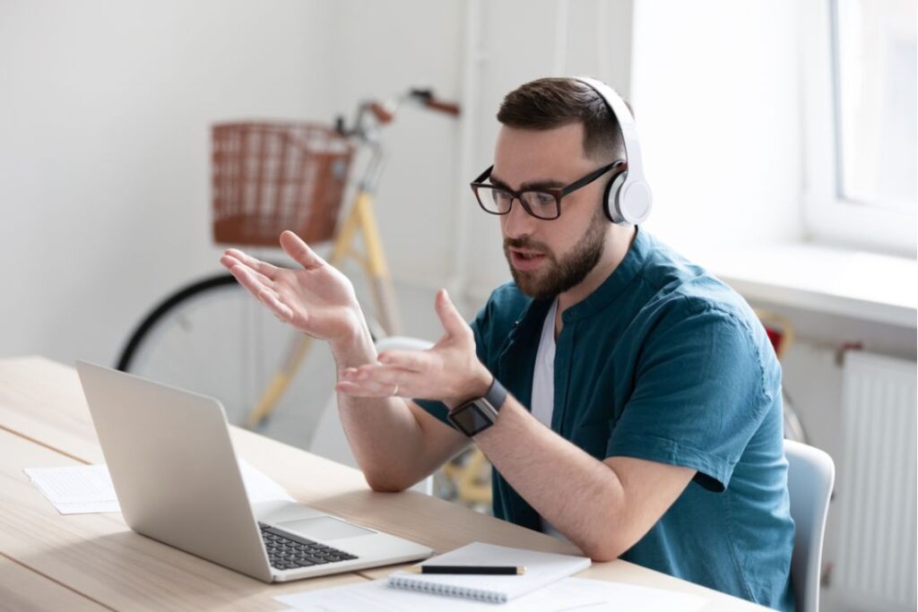 A man wearing an Office Watch gestures while on a video call using his laptop.