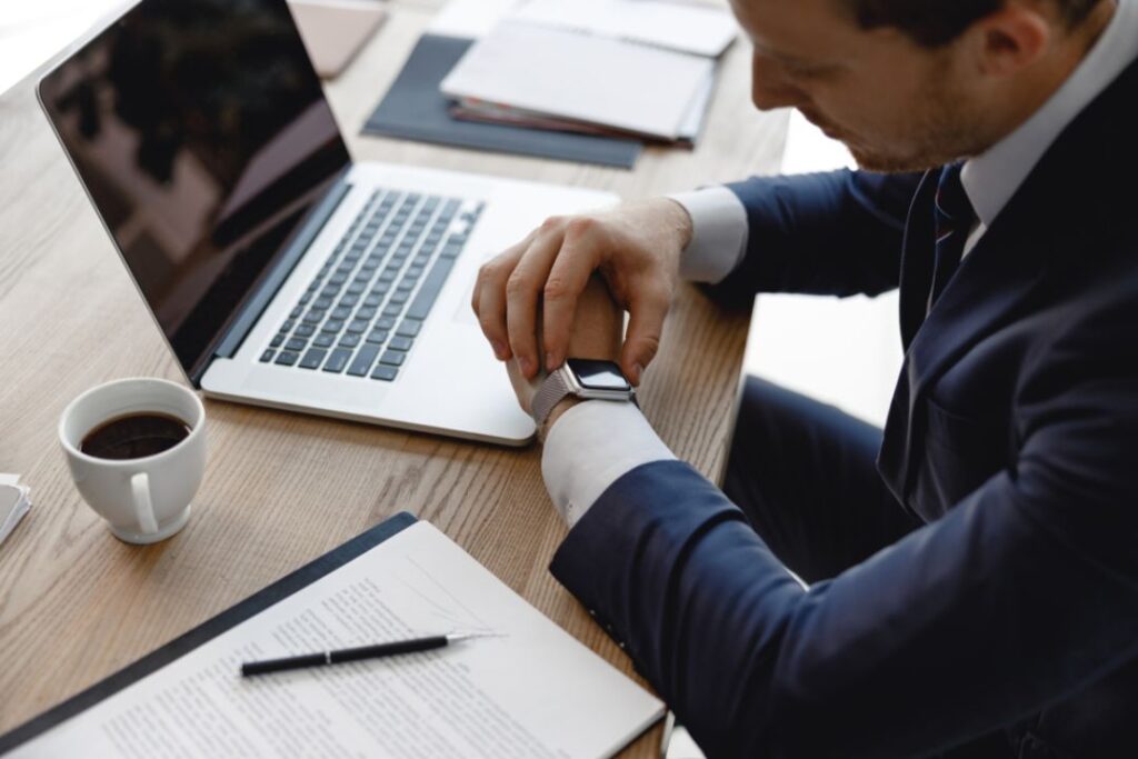 A man in a suit checks his Office Watch at his desk with a laptop and coffee.