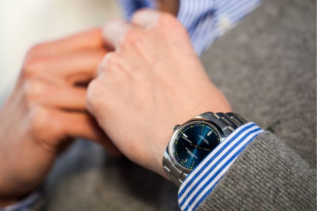 A wrist adjusting a cuff, showcasing a Rolex Oyster Perpetual, embodying Professional watches and impressions. The watch has a blue dial.