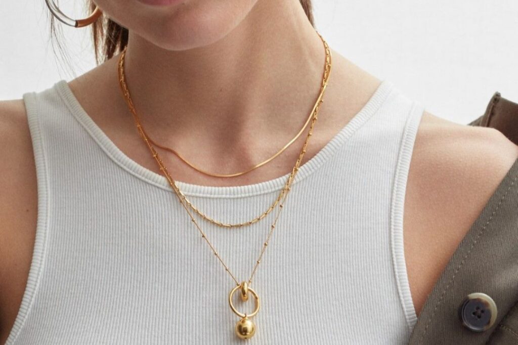 A person wearing layered gold necklaces, showcasing Jewelry and watches with different chain styles and a pendant.