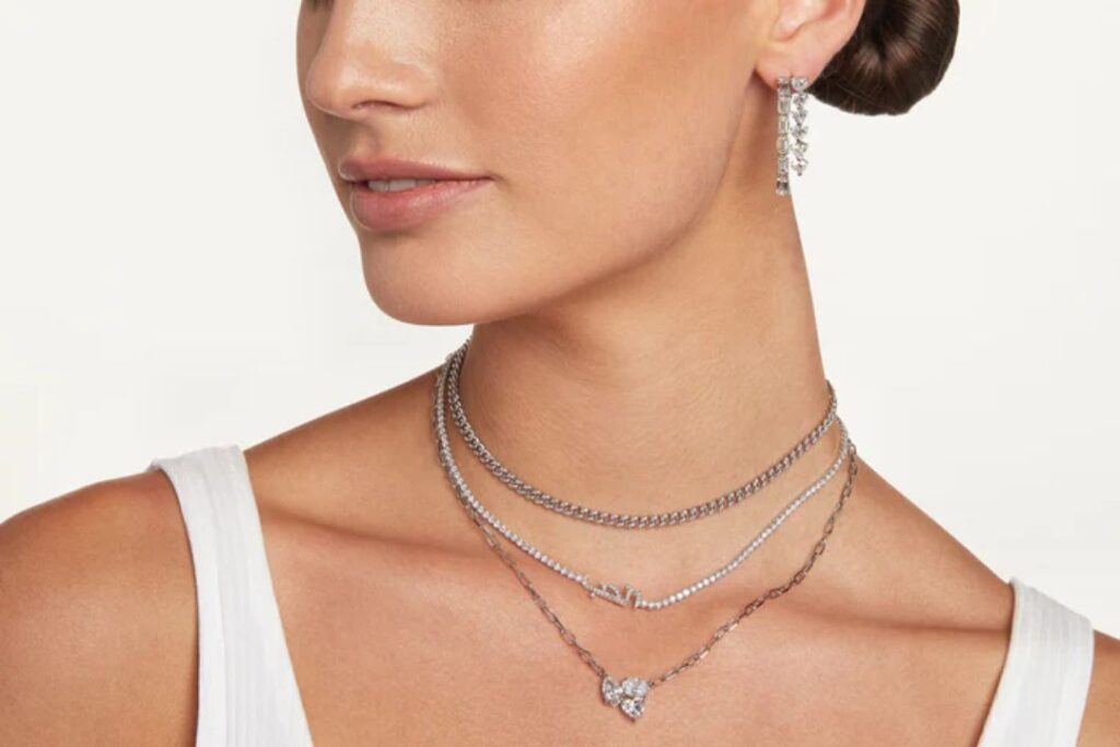 A person displaying Jewelry And Watches: layered necklaces and dangling earrings, against a light background.
