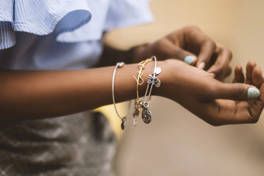 A person with dark skin wearing several bracelets, showcasing Jewelry and watches, including charm bracelets.