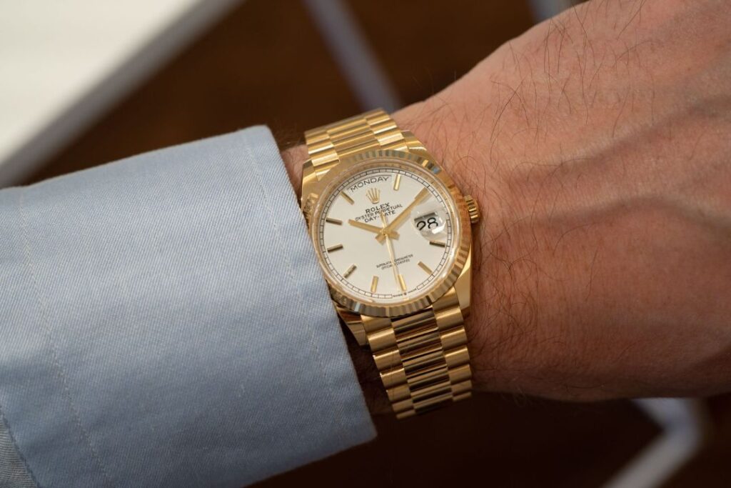 A wrist wearing a gold Rolex Day-Date, a symbol of Professional watches and impressions. It shows "Monday" and the date.