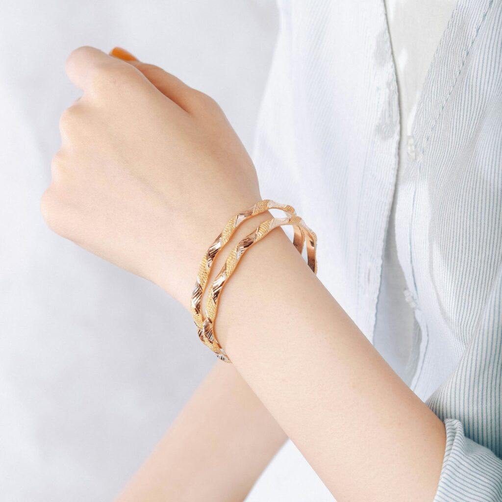 A person's arm wearing two twisted gold bangles, a subtle and elegant choice for Professional Jewelry For Work.