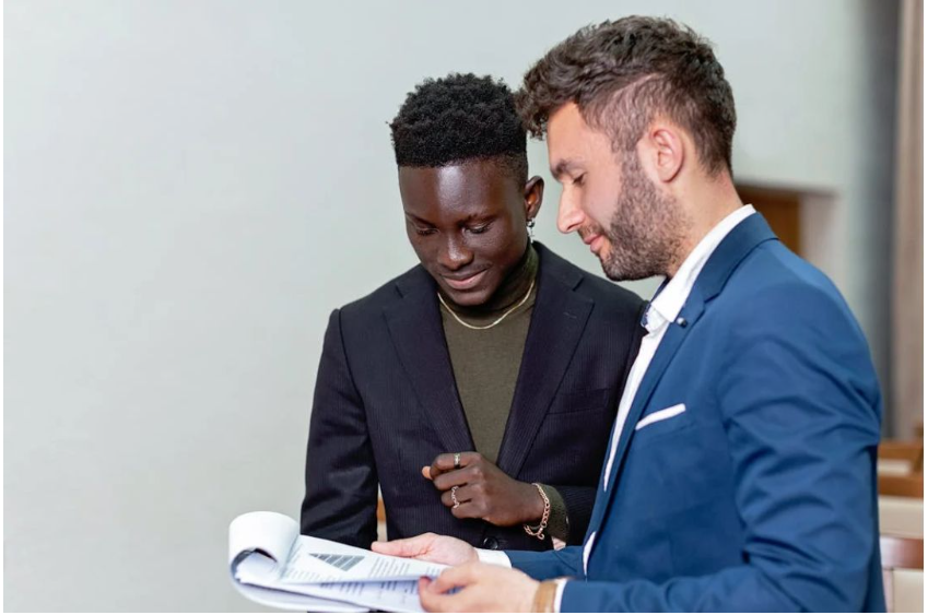 Two professionals reviewing documents. One man wears a subtle chain and ring, suggesting Office Jewelry Essentials.