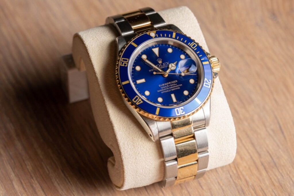 A Rolex Submariner watch with a blue dial and gold accents on a display pillow, a prime example of Jewelry and Watches from Wulf Diamond Jewelers.