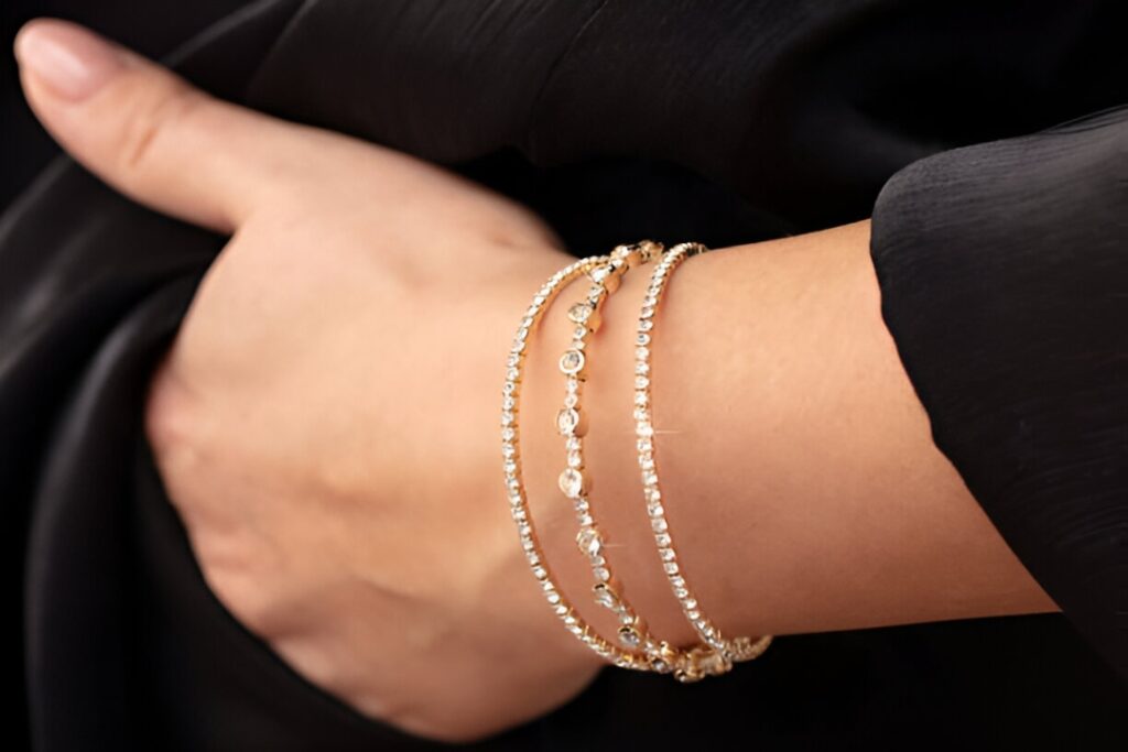 A hand rests on an arm wearing three delicate gold and diamond bracelets, a stunning example of Business Jewelry from Wulf Diamond Jewelers.