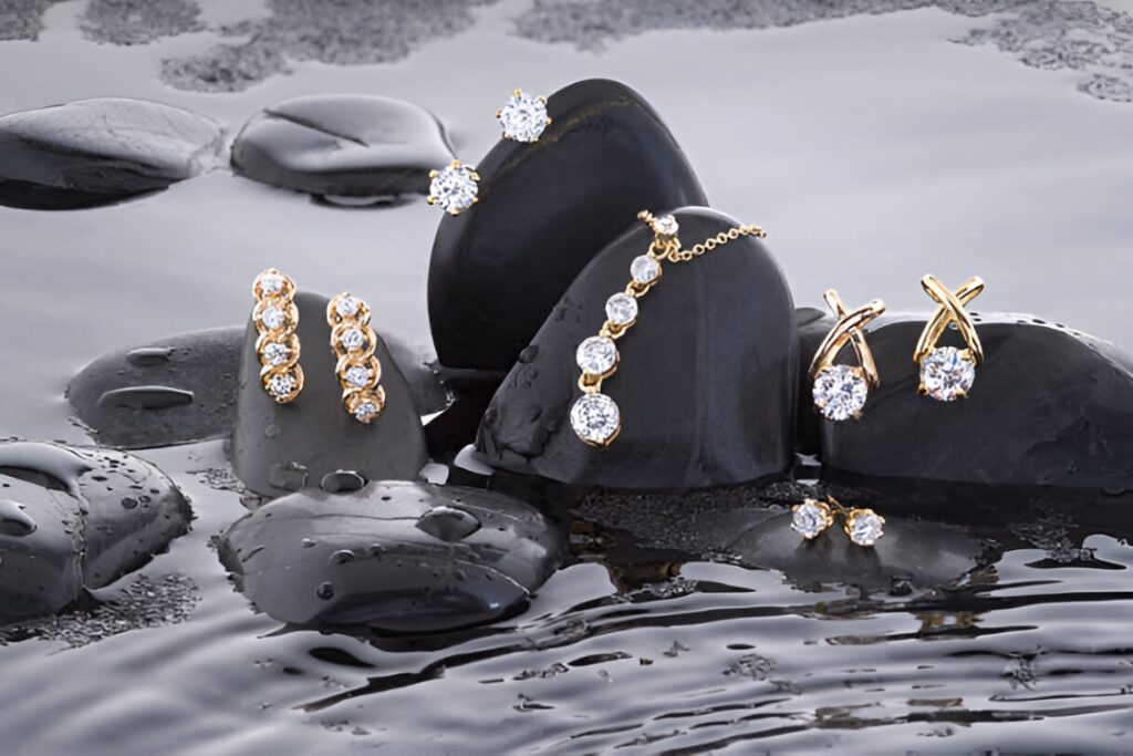 A collection of elegant gold and diamond earrings and a necklace are displayed on wet stones, showcasing sophisticated Business Jewelry from Wulf Diamond Jewelers.