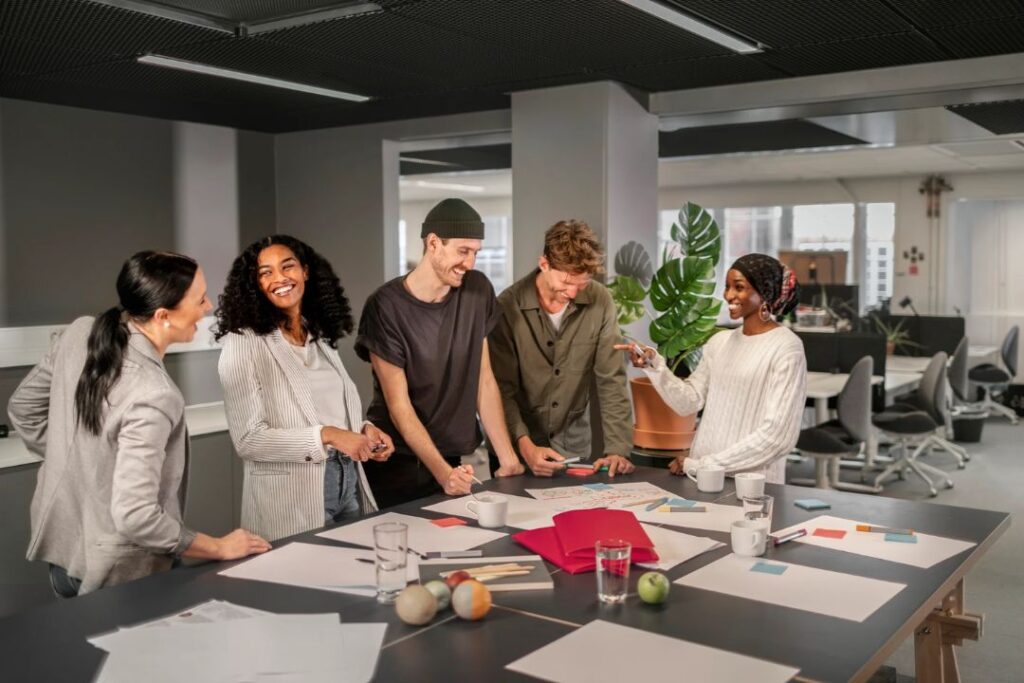 A diverse team collaborates around a table, planning with documents and coffee, enhancing Professional accessories for work.