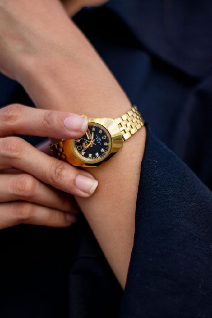 A person's hand adjusts a gold watch, signifying Business Jewelry from Wulf Diamond Jewelers.