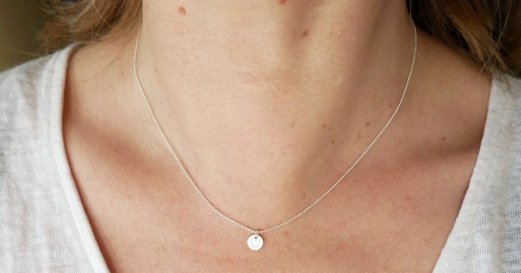A model wears a delicate silver necklace with a tiny circular pendant, showcasing minimalist vacation jewelry by Wulf Diamond Jewelers.