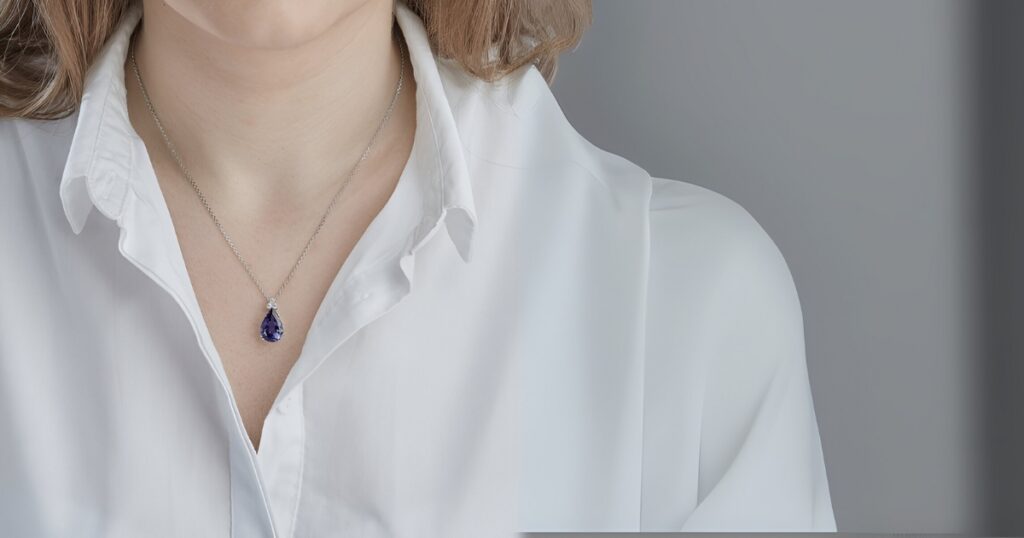 A woman wears a striking purple teardrop pendant on a silver necklace, a piece of minimalist vacation jewelry by Wulf Diamond Jewelers.