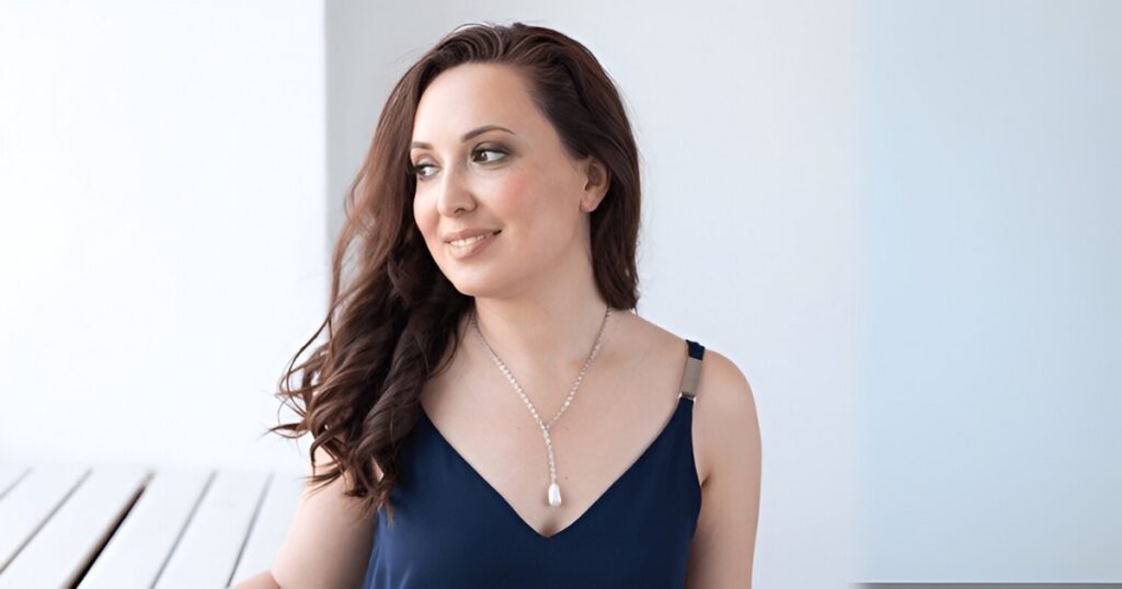 A beautiful model with brown hair wears a delicate Y-shaped pearl necklace, showcasing a piece of minimalist vacation jewelry by Wulf Diamond Jewelers.
