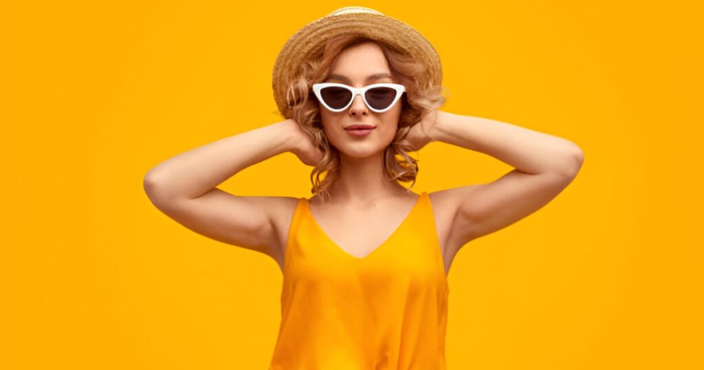 A woman in a swimsuit and sunglasses models Wulf Diamond Jewelers' stylish Summer vacation accessories on a beach.