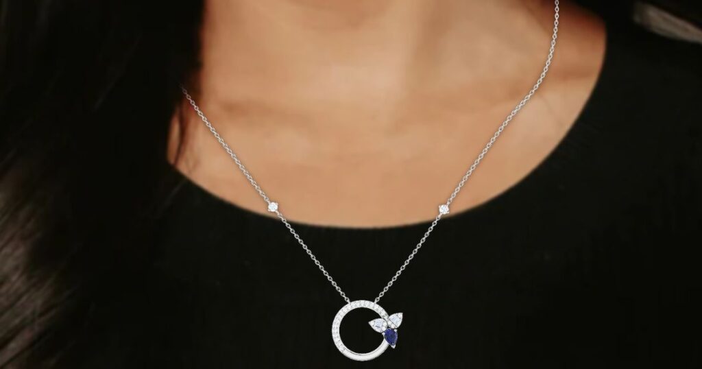 A woman wears a delicate necklace with a circular diamond pendant and blue accents, a piece of Stylish jewelry for holidays from Wulf Diamond Jewelers.