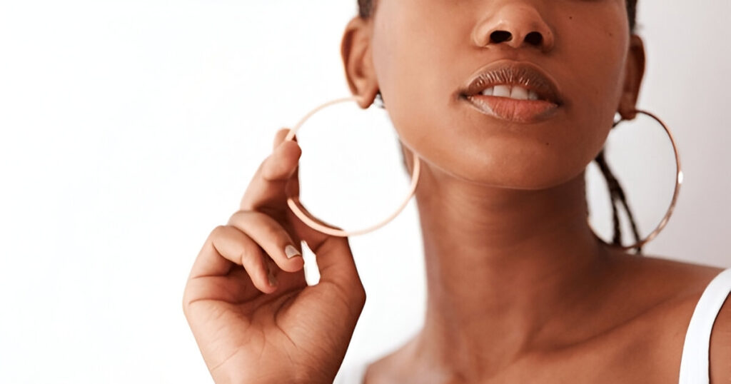 A stylish woman adjusts a large gold hoop earring, representing Wulf Diamond Jewelers' fashionable and elegant Cruise-friendly jewelry.