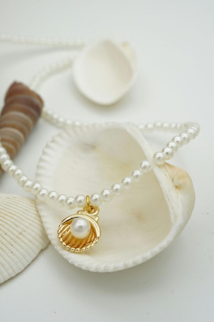 A pearl necklace with a shell pendant sits on seashells, showcasing Tropical jewelry trends by Wulf Diamond Jewelers.
