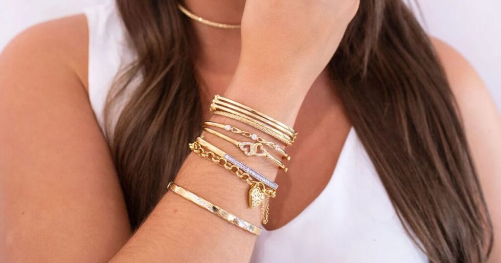 A woman's arm with layered gold and diamond bracelets, a prime example of Wulf Diamond Jewelers' Beach jewelry essentials.