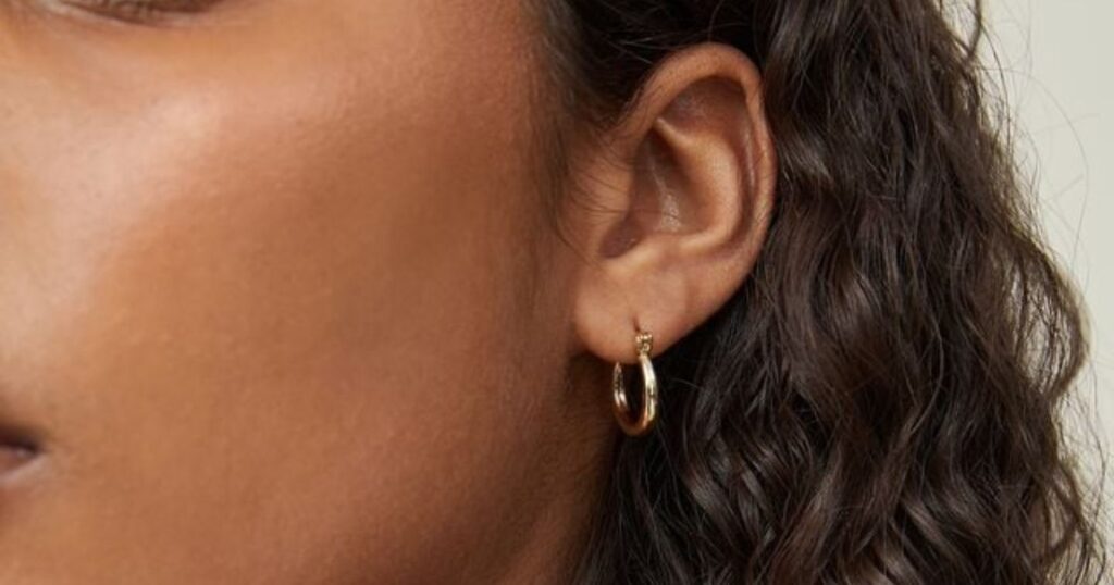 Close-up shot of a model wearing a small, elegant gold hoop earring, showcasing minimalist vacation jewelry by Wulf Diamond Jewelers.