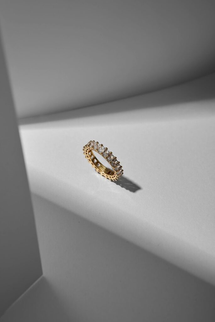 Elegant gold diamond eternity band placed on a white surface, showcasing stylish jewelry for holidays with timeless sparkle and charm.