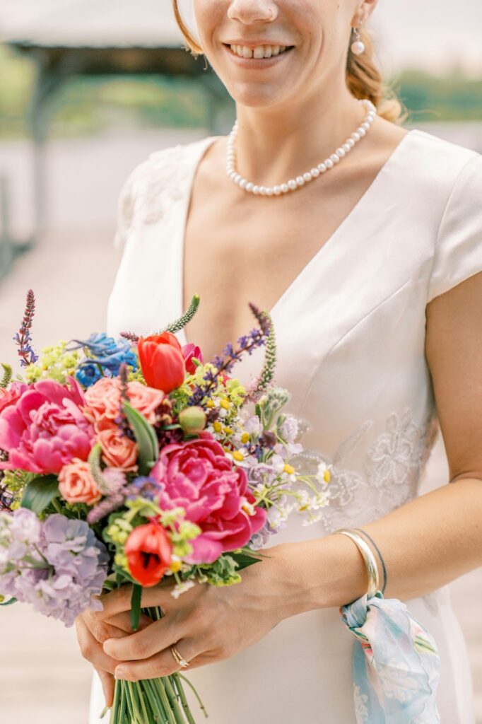 A young woman on a beach smiles with a straw hat and gold necklace, symbolizing Wedding jewelry for destination events by Wulf Diamond Jewelers.