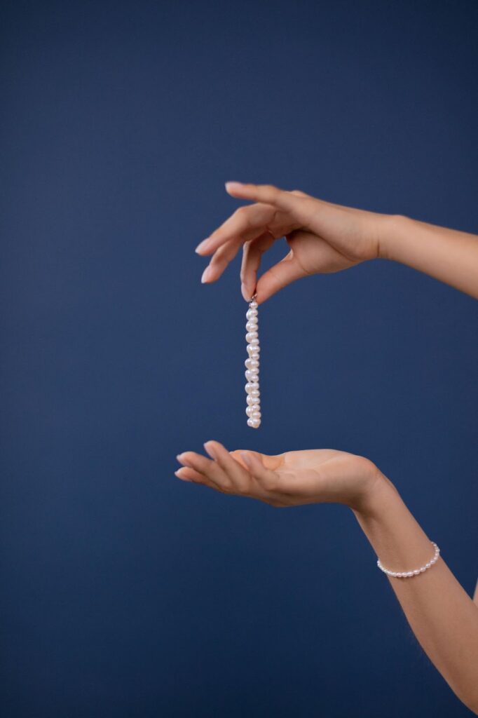 A pair of hands gently holding a delicate pearl necklace, with another pearl bracelet on the wrist below, suggesting effortless style when packing jewelry for vacation with Wulf Diamond Jewelers.