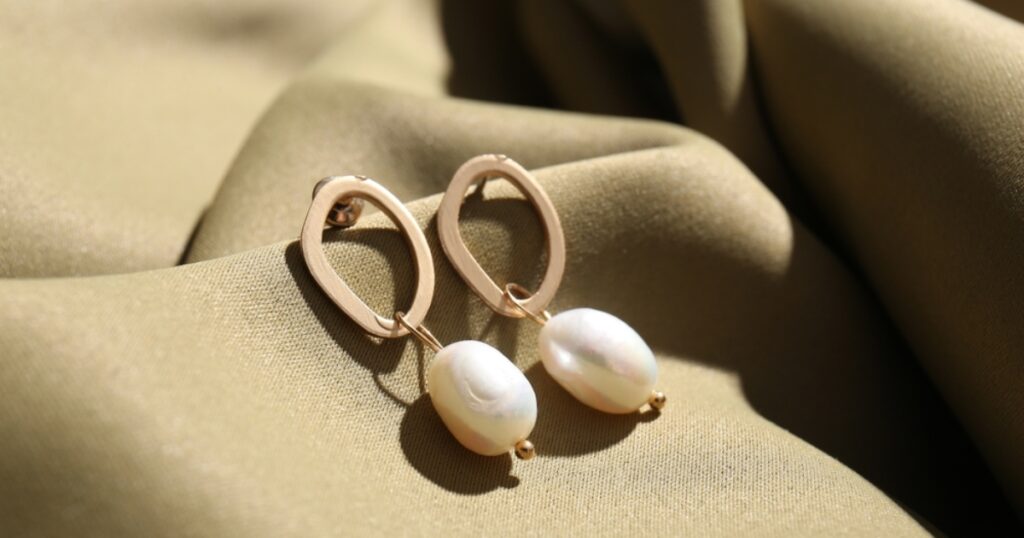 Gold-toned earrings with a modern, free-form shape and large pearl drops, perfect for a chic look when packing jewelry for vacation from Wulf Diamond Jewelers.