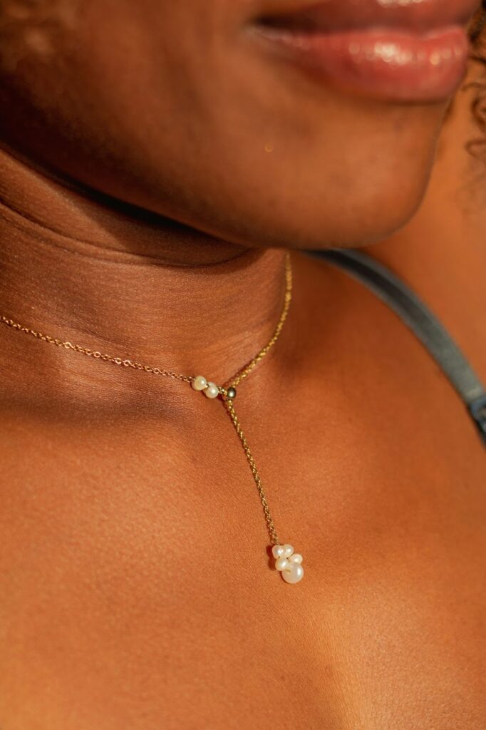 A close-up of a model's neck, showing a delicate lariat necklace with a cluster of pearls, a perfect choice for lightweight travel necklaces from Wulf Diamond Jewelers.