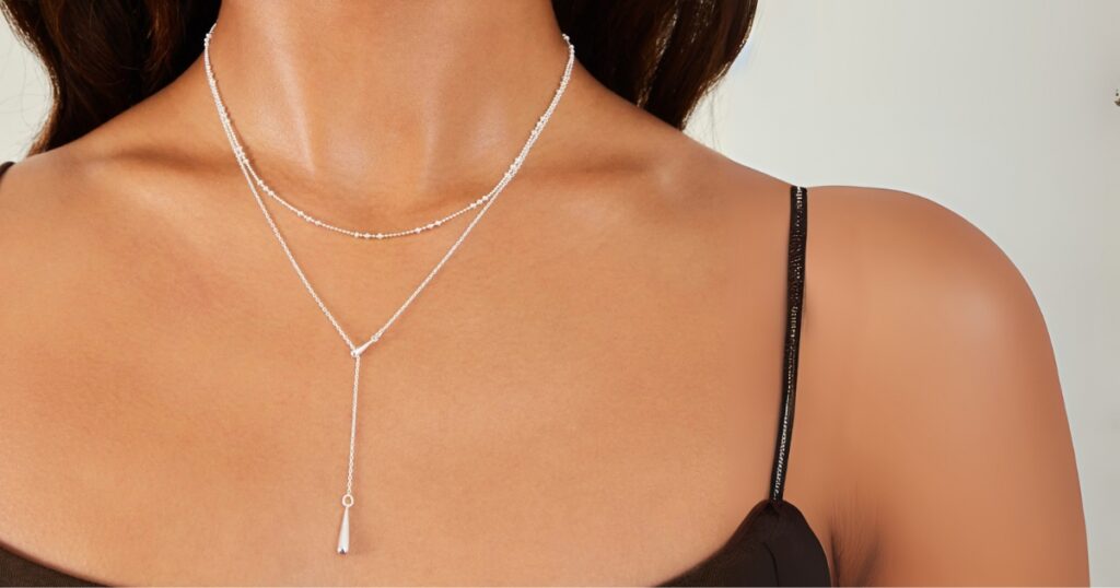 A model showcases layered silver necklaces, including a lariat with a teardrop pendant, a perfect choice for lightweight travel necklaces from Wulf Diamond Jewelers.