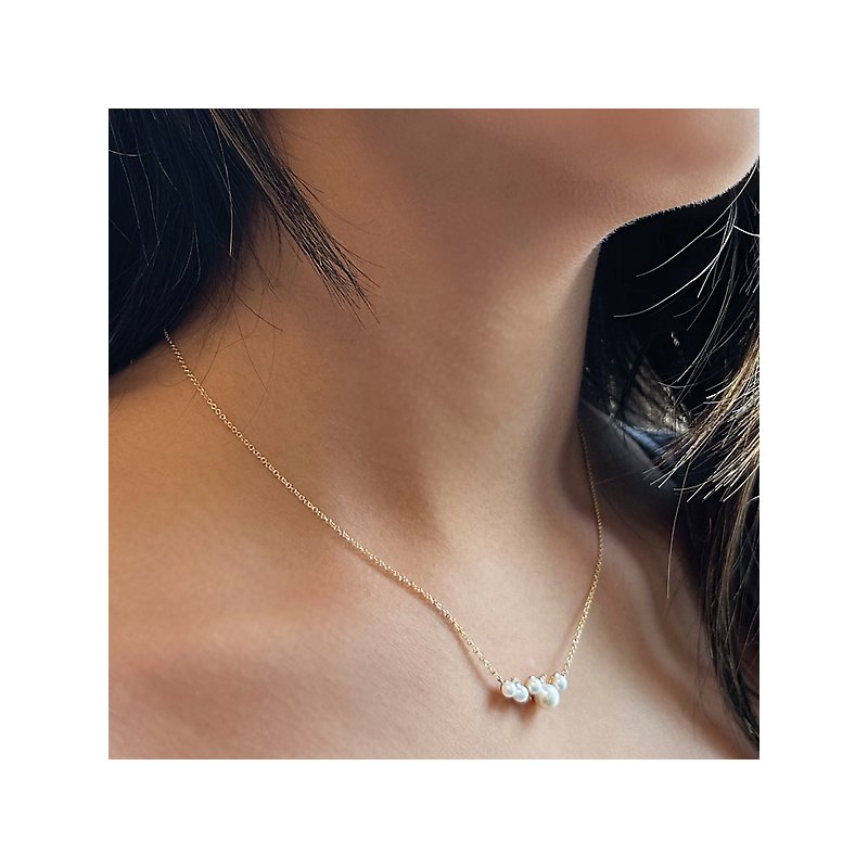 A close-up of a model's neck and shoulders, showing a delicate gold chain with three small pearls, a perfect choice for lightweight travel necklaces from Wulf Diamond Jewelers.
