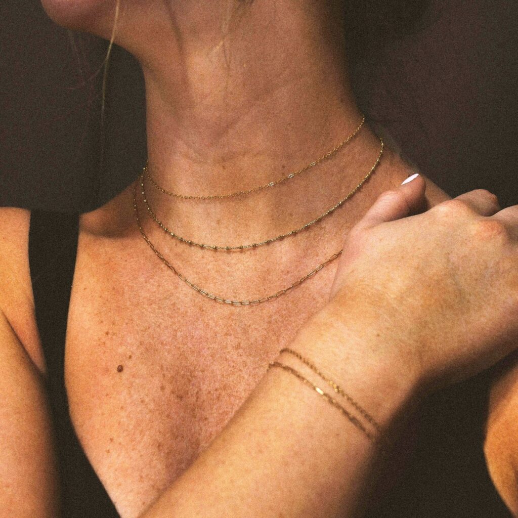 A close-up of a model's neck and chest, showing three layered necklaces and a bracelet, featuring lightweight travel necklaces by Wulf Diamond Jewelers.