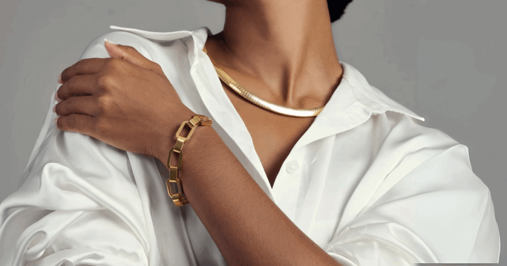
A model wears hypoallergenic jewelry for travel, including a gold bracelet and necklace, over a white silk blouse from Wulf Diamond Jewelers.